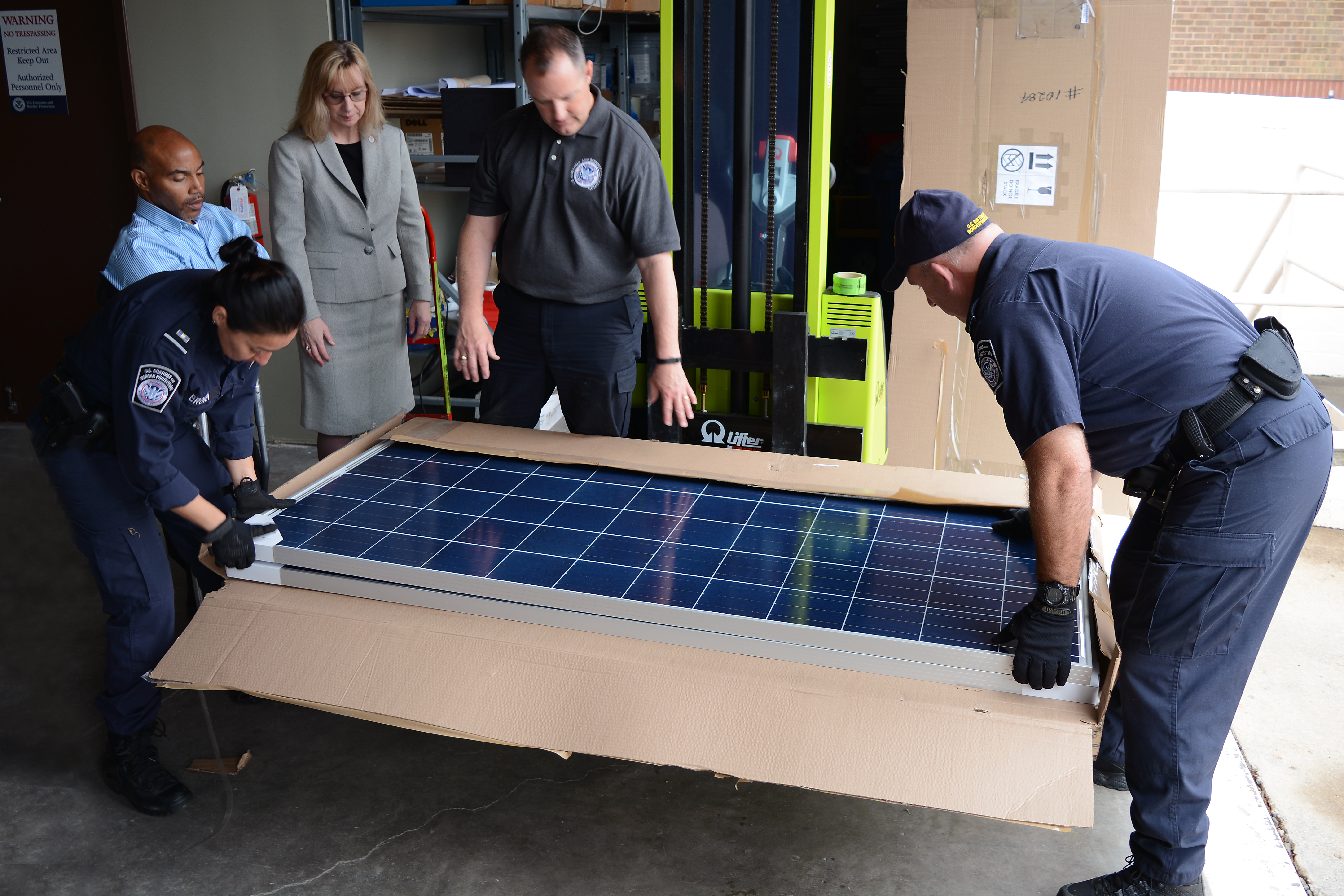 CBP Officers Joyce Brown and Robert Boswell lift a solar panel from its shipping carton as the import specialist team, Wilbert Jones, Laurie Pazzo and Jeff Sorrells, discuss sending a sample to the CBP lab. Photo by Scott Sams