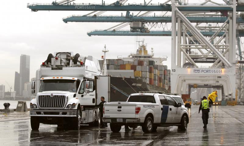 A U.S. Customs and Border Protection officer, right, shakes off his rain coat as he and a fellow officer wrap up scanning of shipping containers as they inspect incoming cargo at the Port of Miami in Miami, Florida. Photo by Glenn Fawcett