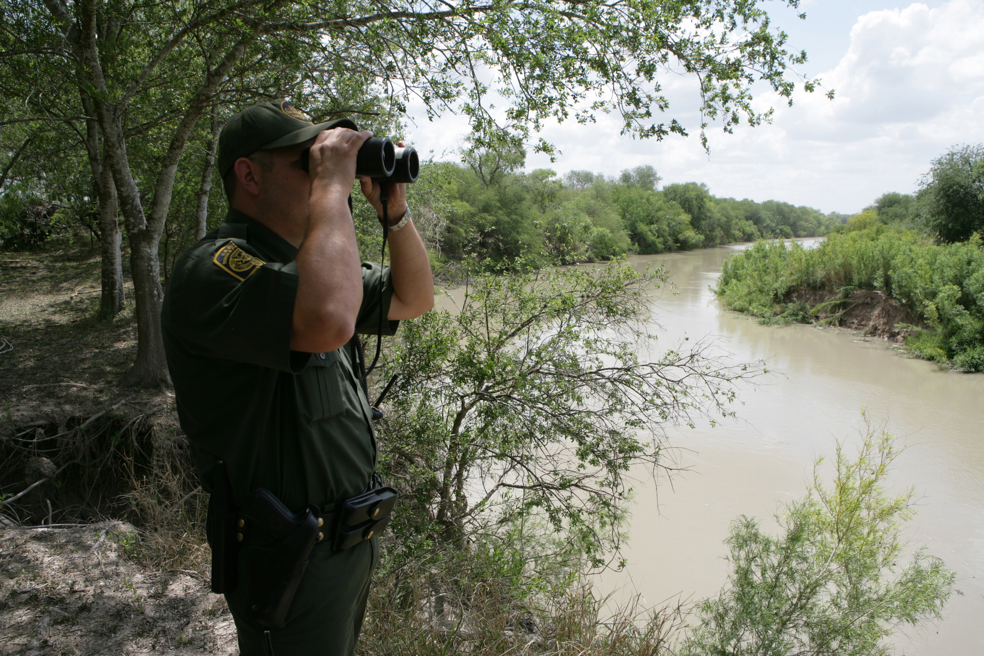 U.S. Border Patrol agent scans the area into Mexico with binoculars looking for illegal immigrants potentially staging to enter the United States.