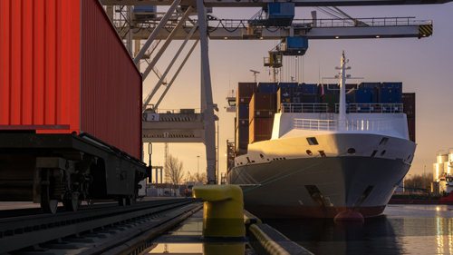 Shipping container in rail track next to docked cargo ship..