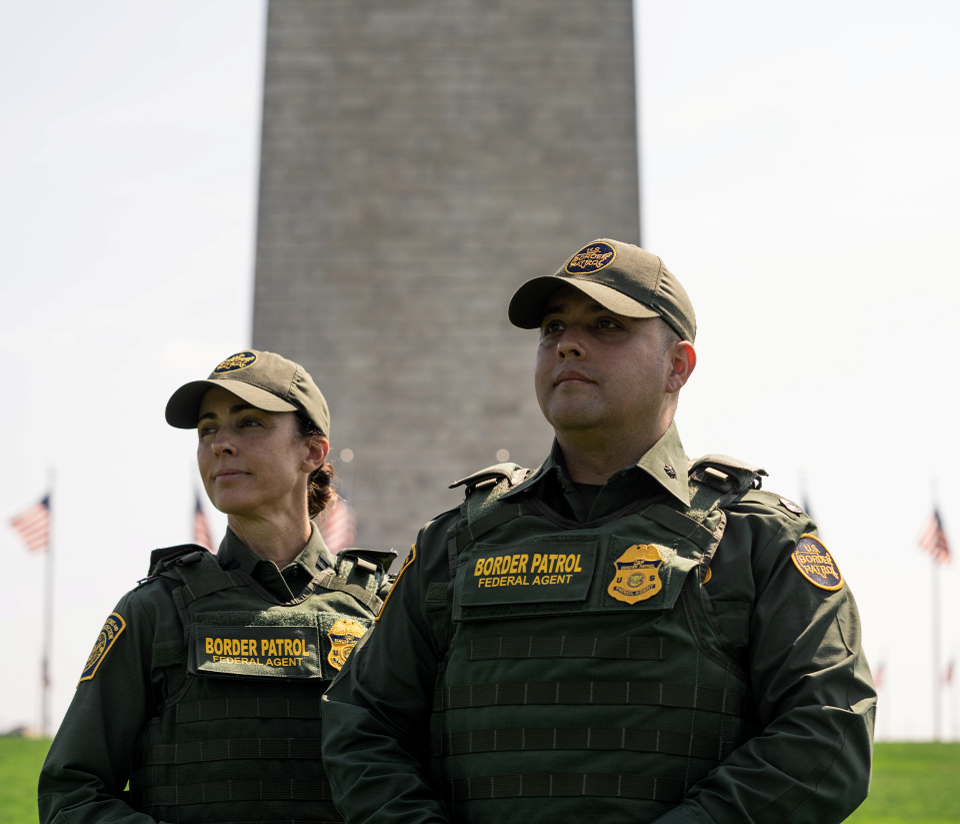 One Female and One Male Border Patrol Agent standing side by side in front of Washington Monument