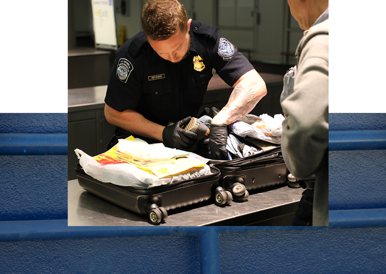 Male CBP Officer inspecting a passenger's luggage at an airport