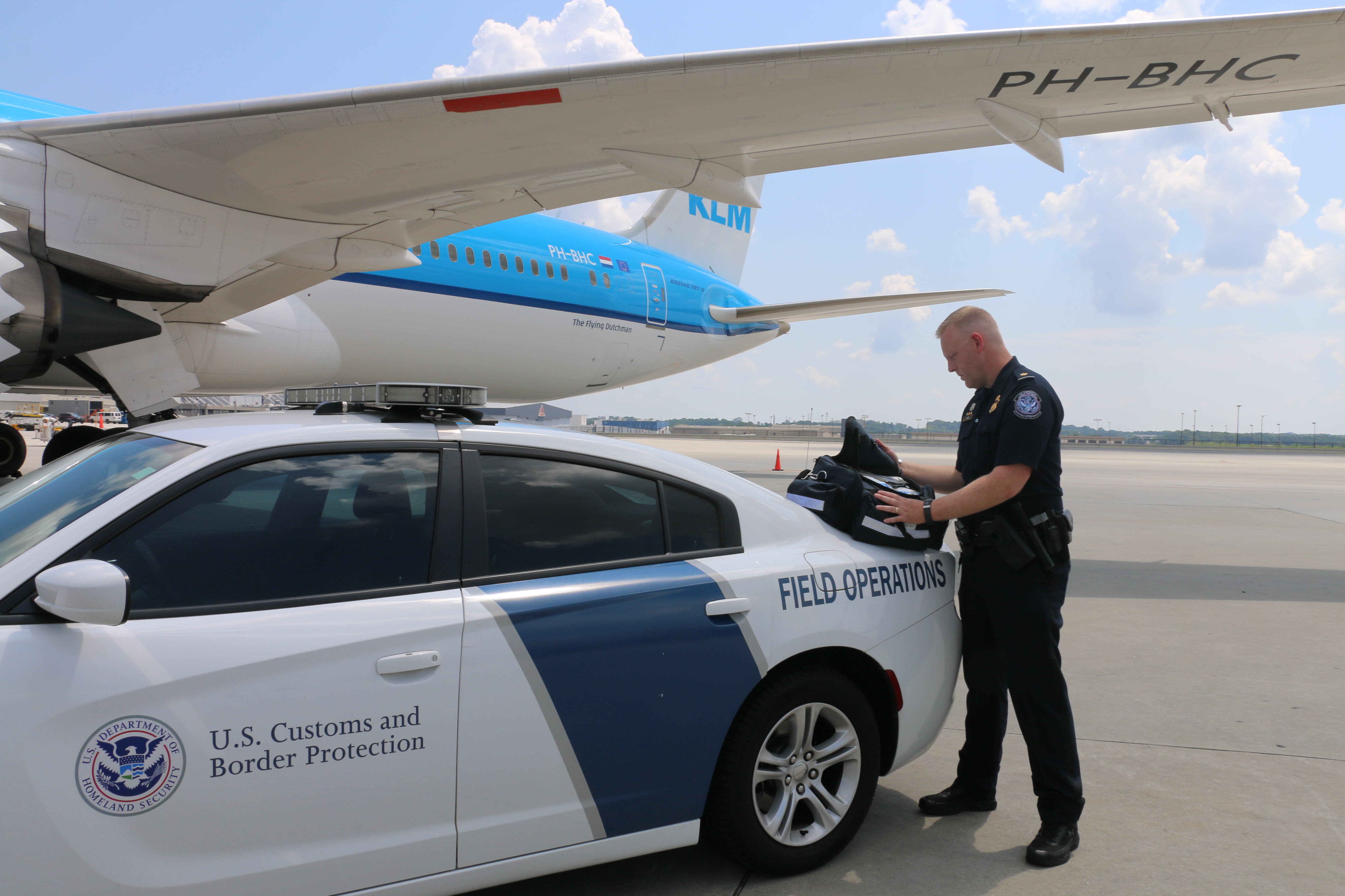 CBP officer in front of CBP vehicle and aircraft on tarmac at Atlanta.