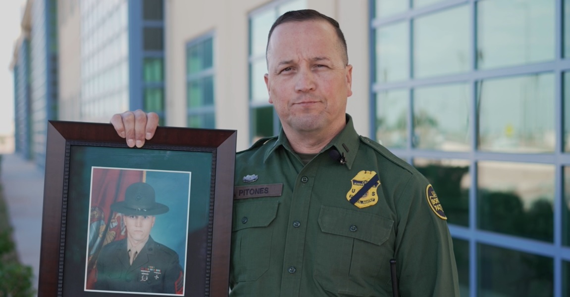 A CBP veteran holding up a framed photograph of himself as a young officer.