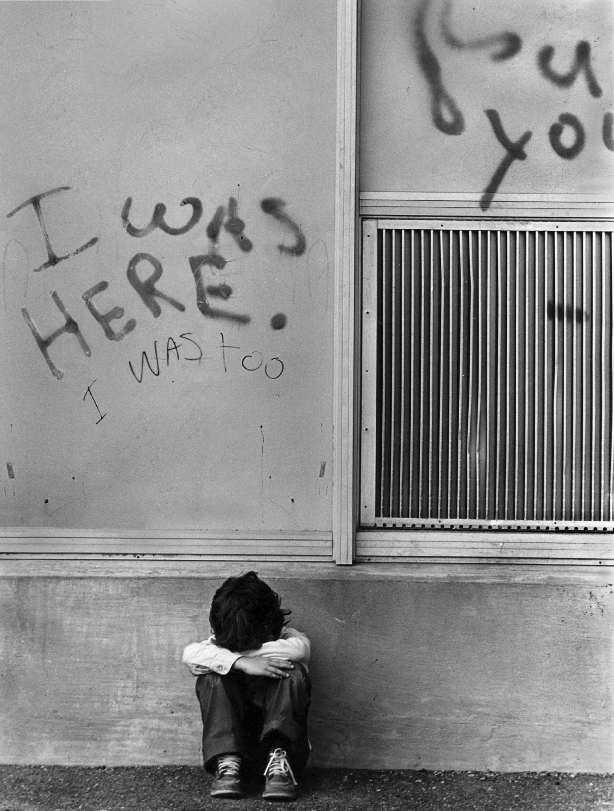 A small child is photographed sitting on the curb with his head in his hands.