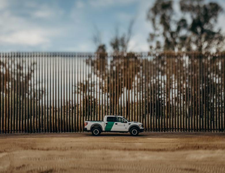 A Border Patrol truck drives along the U.S.-Mexico border in front of a bollard-style fence.
