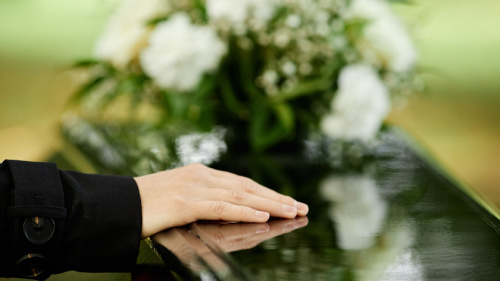 Close up of female hand on coffin saying goodbye at outdoor funeral ceremony