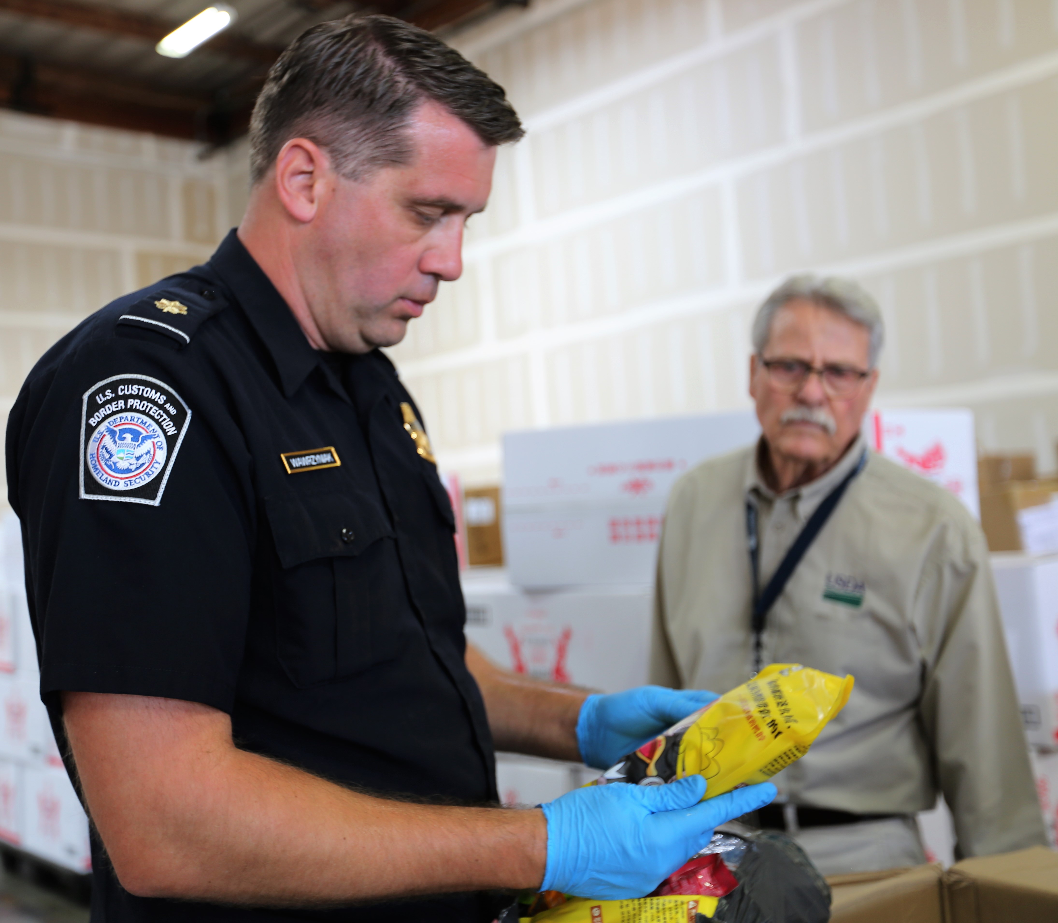 A CBP supervisory agriculture specialist, left, examines a pork soup mix while a veterinary medical officer from USDA’s Animal Plant Health Inspection Service looks on. 