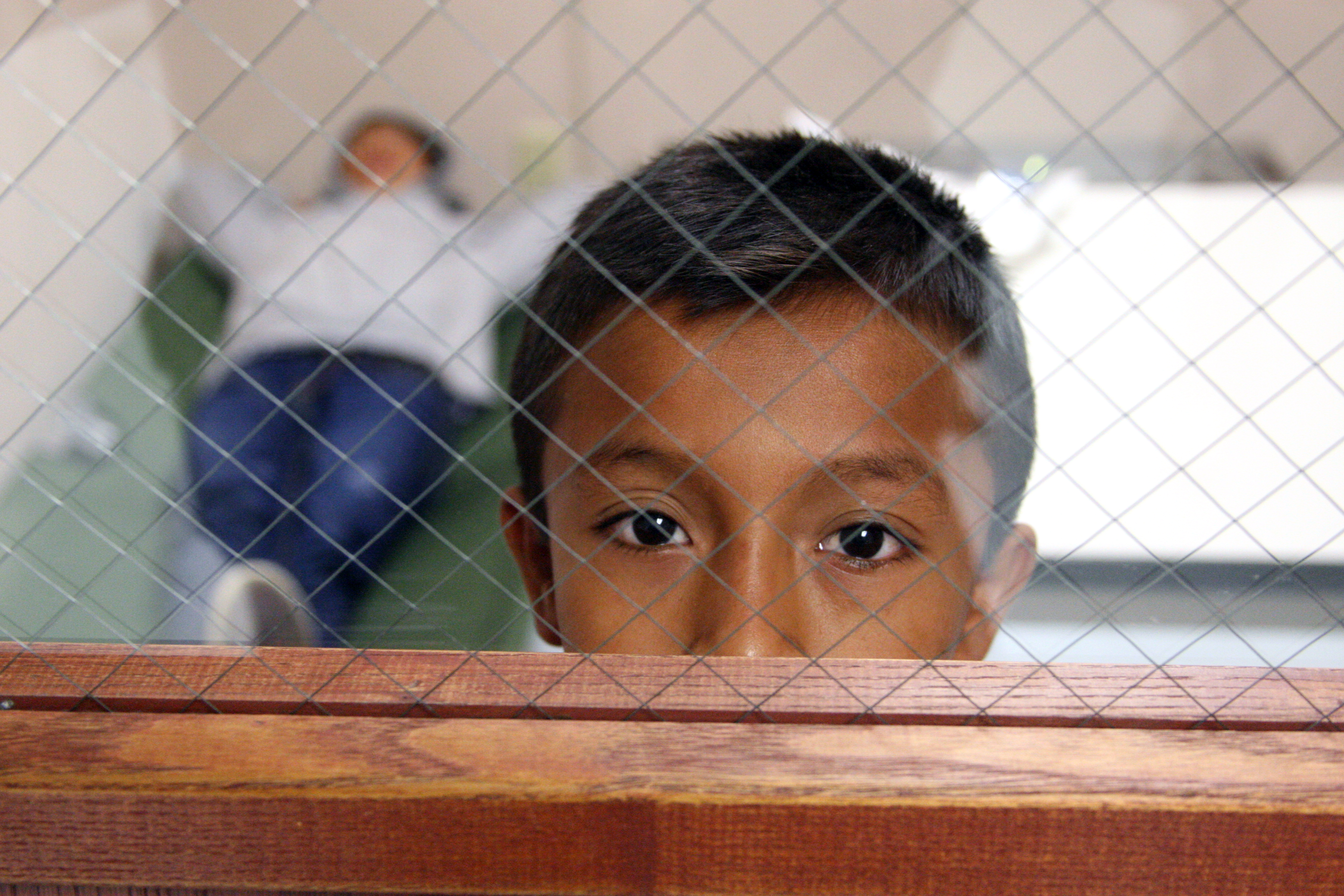 A youngster looks out the door window from the room he is staying in at the Brownsville, Texas port of entry. (Photo by Eduardo Perez)