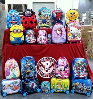 Child backpacks lined up after a CBP seizure. Table cloth is maroon wit the CBP seal on it. 