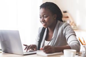 Black woman sitting at desk, typing on Laptop, smiling