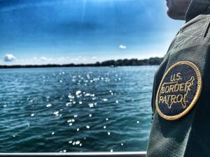 Border Patrol agent standing along the St Clair River with shoulder patch showing