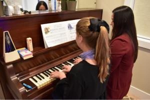 Senior Auditor Ana Rodriguez is pictured with a student playing the piano. 