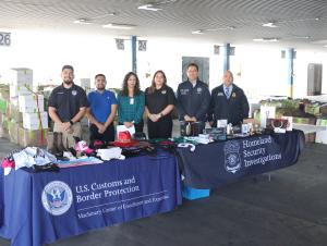 CBP import specialists and HSI special agents are flanked by a display table of previously seized counterfeit items during a Christmas holiday shopping safety outreach event hosted at Laredo's World Trade Bridge.