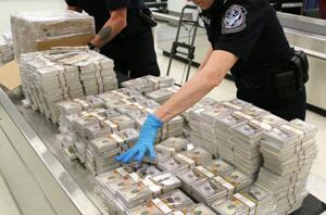Stacks of counterfeit currency with a CBP Officer sorting it behind the currency