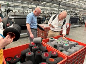 Two individuals looking at spools of yarn in a factory. 