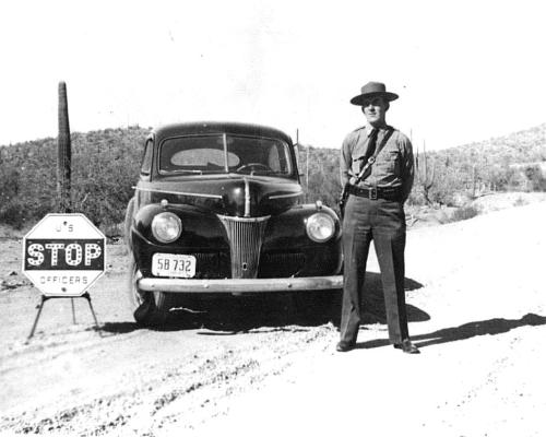 Border Patrol Agent stands next to border patrol vehicle at checkpoint.