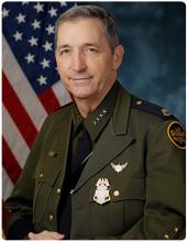 Benjamine “Carry” Huffman, CBP Acting Deputy Commissioner seated in front of a blue background with a flag to the left.