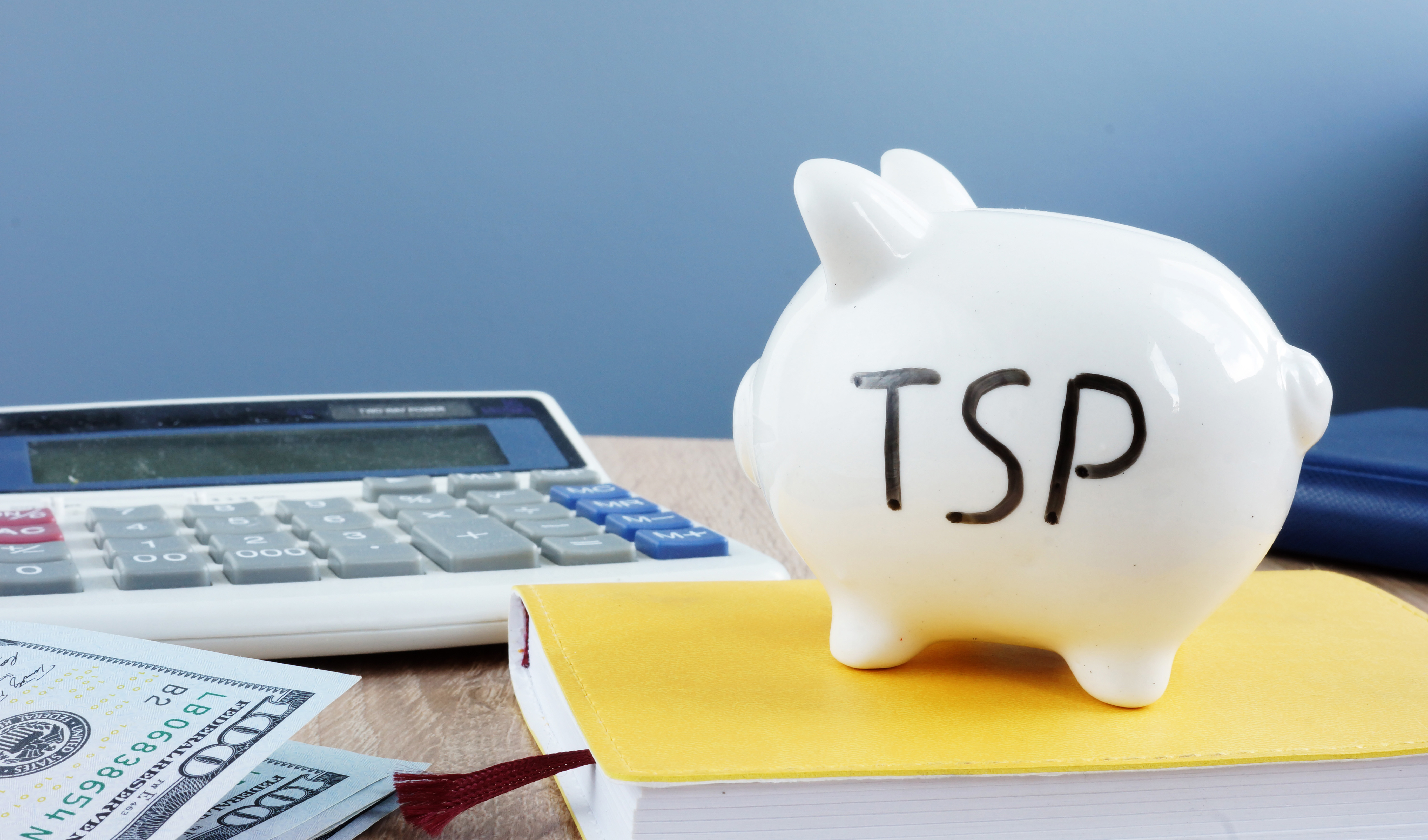 White piggy bank with "TSP" written on its side resting next to a calculator.