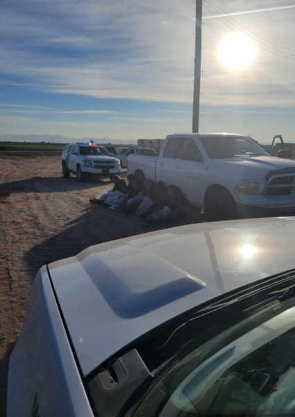 Six individuals seated on the ground next to a white 2011 Dodge Ram