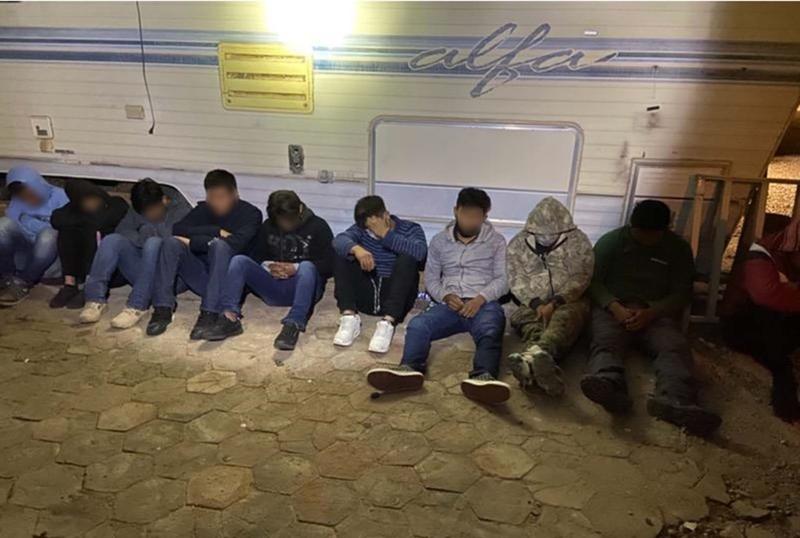 14 undocumented persons sit outside of trailer they were found in.