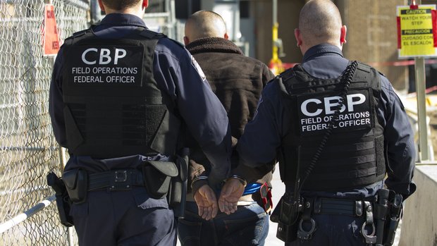 Oficiales de CBP escoltan una persona buscada bajo un orden de arresto.