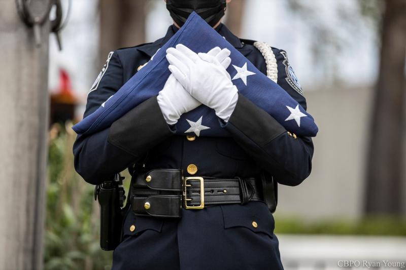 Un miembro de CBP Operaciones Aduaneras Guardia de Honor lleva una bandera americana doblada.