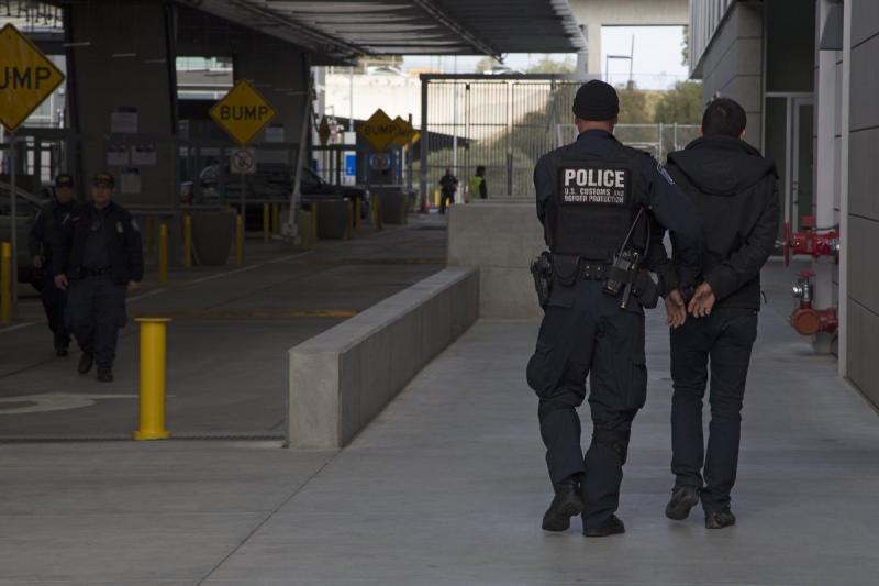 A CBP officer escorts a wanted person at a U.S. port of entry.