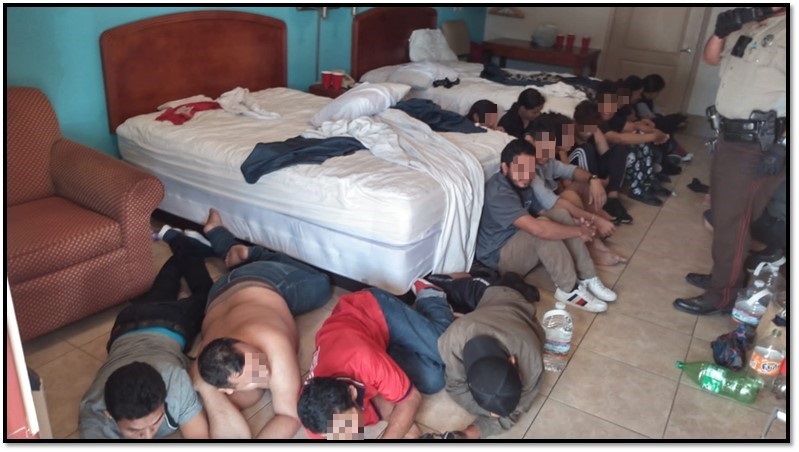 Migrants in crowded hotel room.