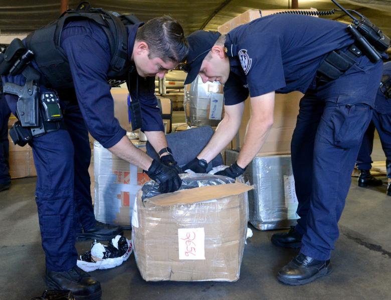 Coast Guard (left) and Customs and Border Protection officers examine a box in a shipping container. Wilmington, Del., CBP and USCG discovered 368 rounds of ammo concealed inside a container bound for Guatemala August 27, 2017.