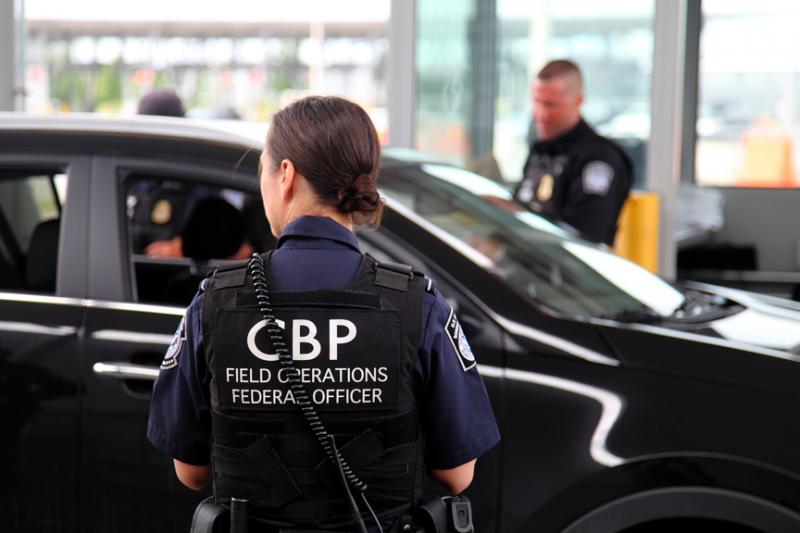 CBP officer speaking with passengers inside a vehicle at a CBP port of entry.