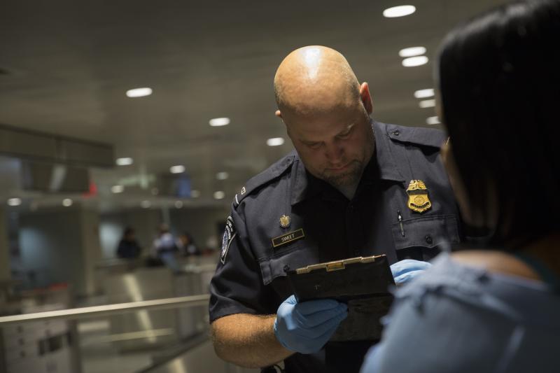 CBP Officer looks at clipboard while passenger passes before him