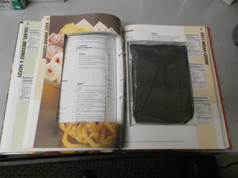 Inside of cookbook, with it opened to show cut out area with dark package of cocaine placed inside